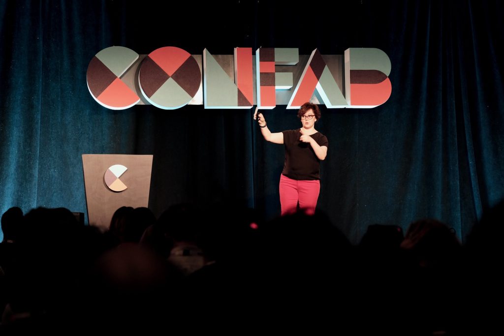 Kristina Halvorson raising her hand on stage with Confab 2019 letters behind her