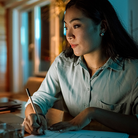 Young woman in light blue shirt with a pen in hand, writing on a piece of paper.