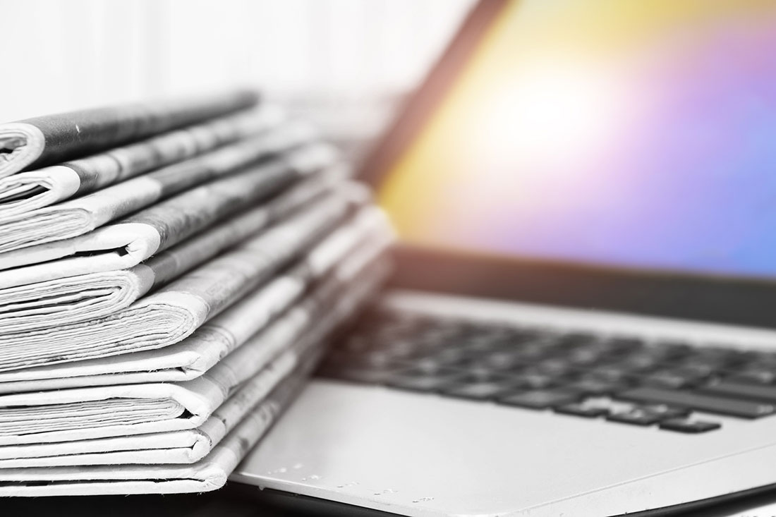 Stack of newspapers next to a laptop.